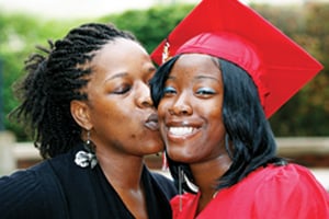 Woman kissing her daughter who is in a red graduation gown.